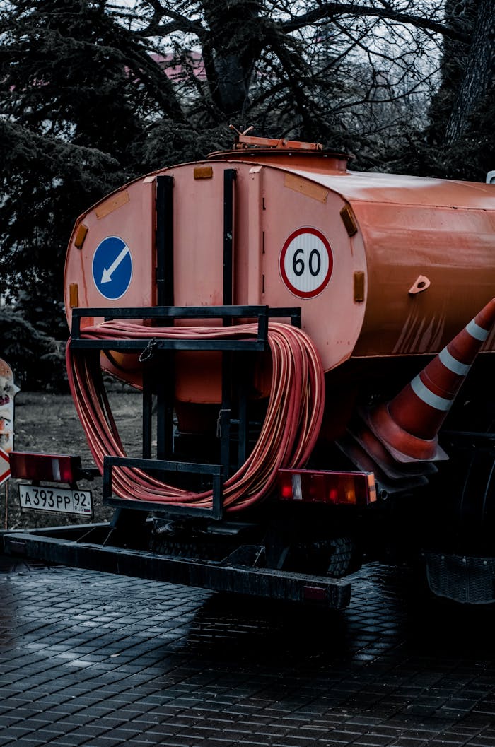 Orange service vehicle with hoses and traffic cones in an urban setting, depicting public utility work.