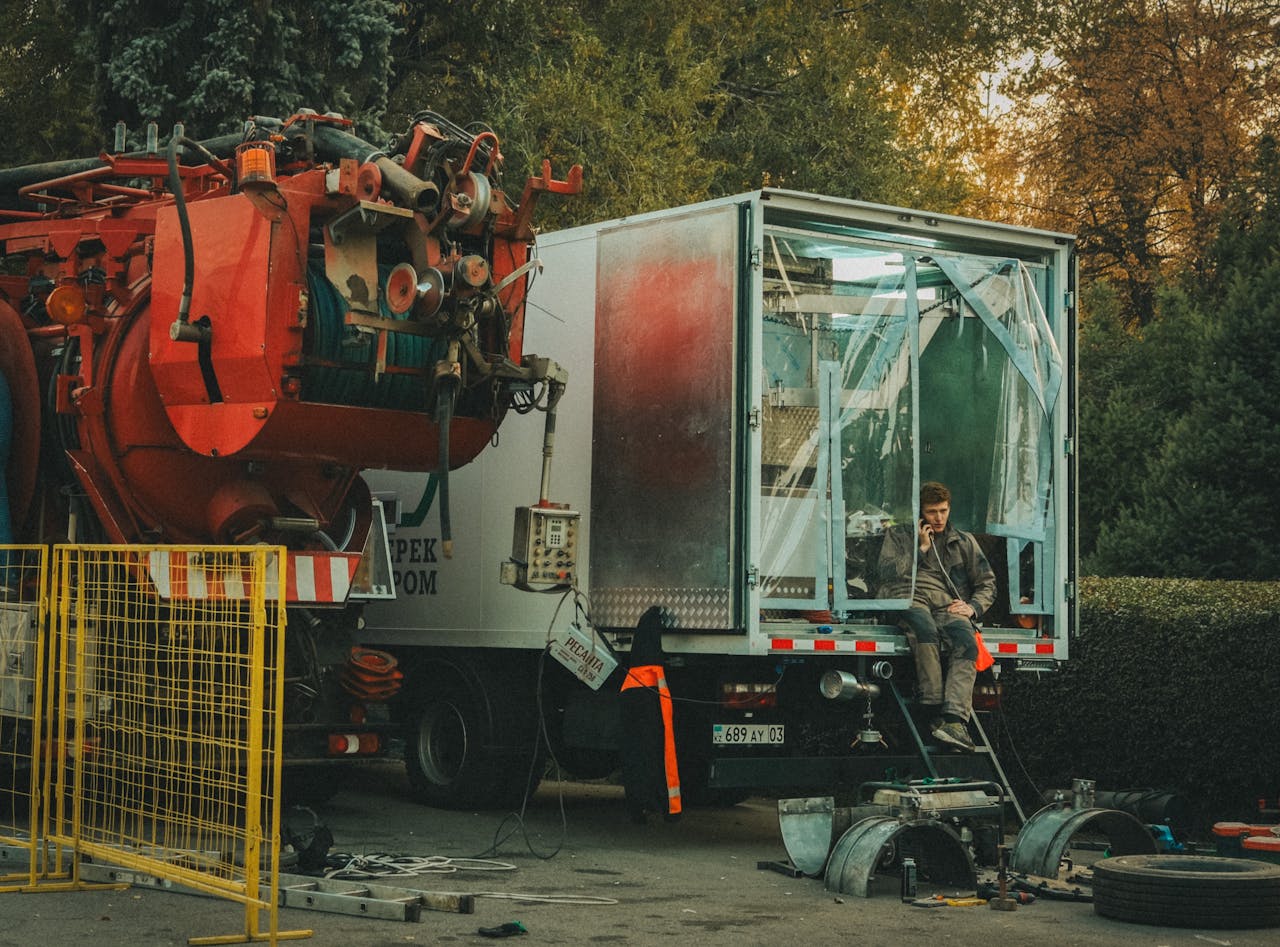 A worker repairing an industrial truck in an outdoor setting, surrounded by tools and equipment.