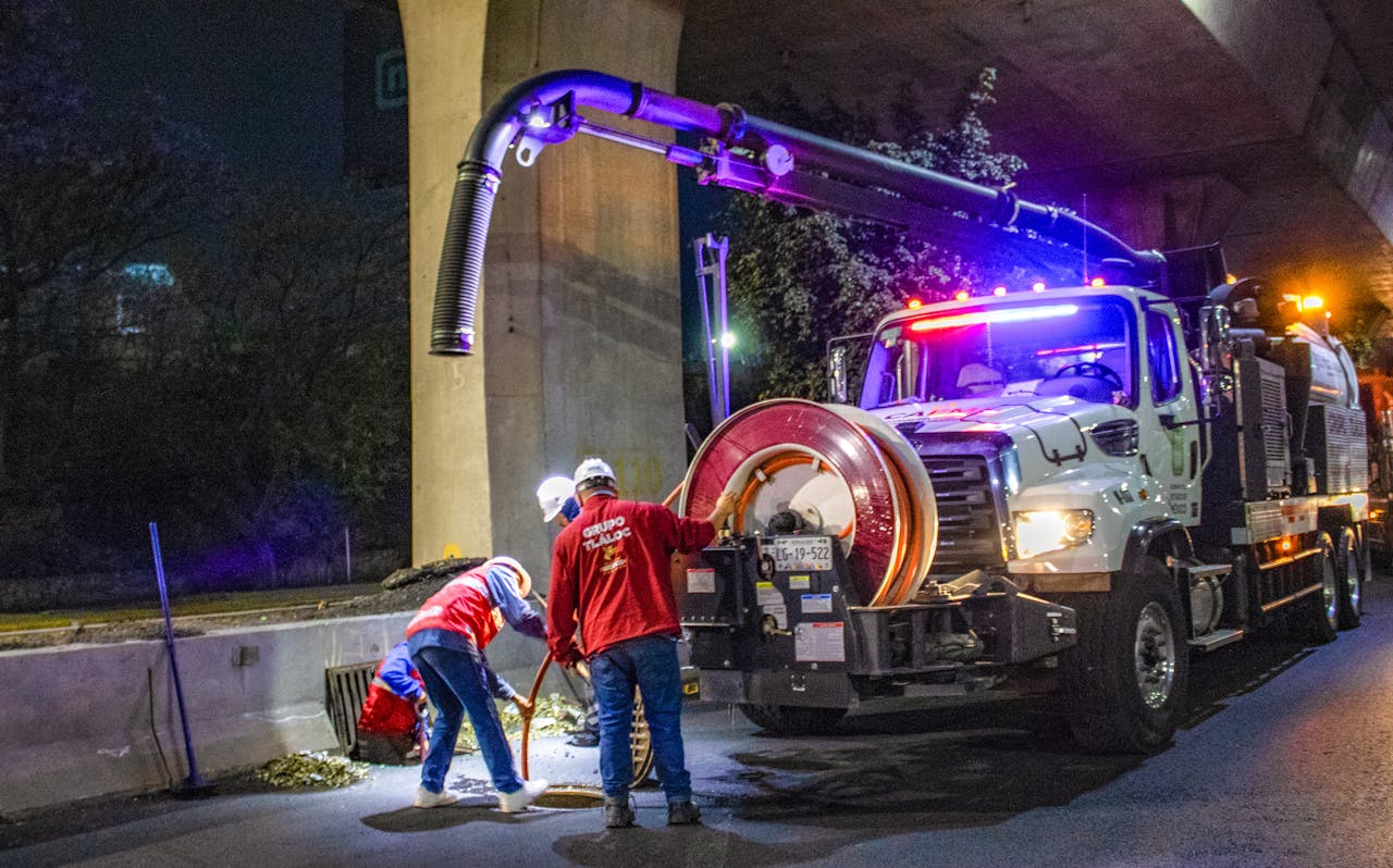 Workers performing maintenance at night using specialized machinery under a bridge.
